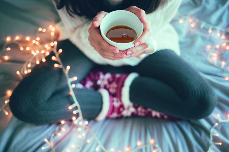 Woman sitting at home legs crossed on bed, holding a cup of coffee, christmas decoration.