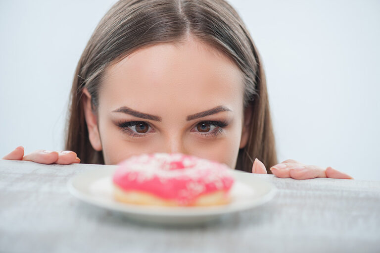 Beautiful girl is looking at unhealthy donut with appetite. It is situated on a table. Isolated on a white background; Shutterstock ID 284988062