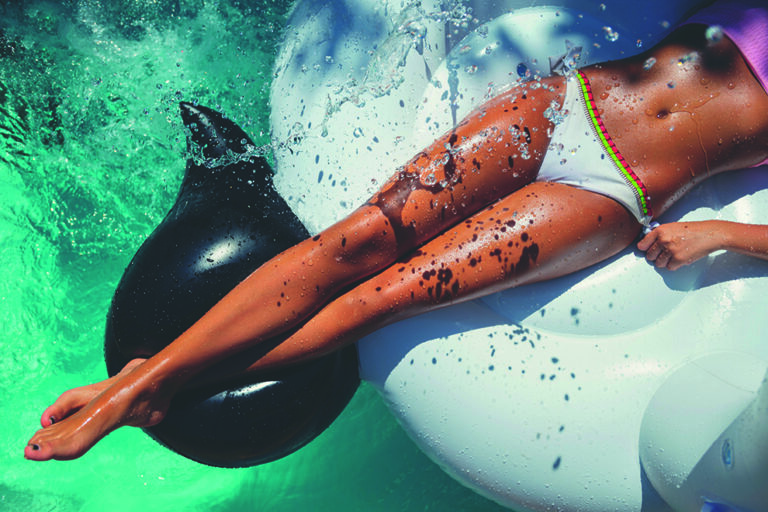 Woman floating on a white inflatable in swimming pool in a white bikini. Tight crop showing only her legs and feet. She is tanned in turquoise water with water splashing onto her. Woman floating on a white inflatable in swimming pool in a white bikini. Tight crop showing only her legs and feet. She is tanned in turquoise water with water splashing onto her.