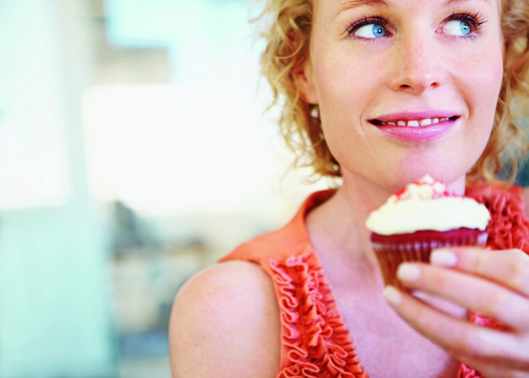 A pretty young woman holding a cupcake and looking away happily A pretty young woman holding a cupcake and looking away happily