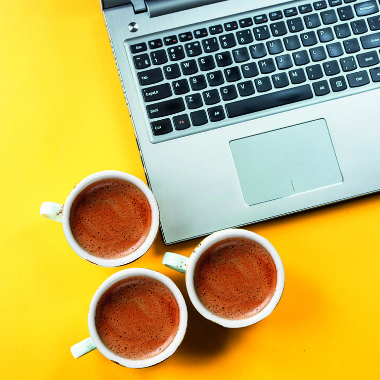 Smile emoji painted on cups of cappuccino next to the laptop on a yellow background. Emotions and communication online concept Smile emoji painted on cups of cappuccino next to the laptop on a yellow background. Emotions and communication online concept