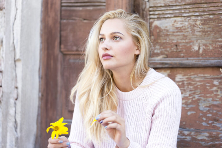 girl with a pink sweater pulling a daisy leaf in front of an wooden door