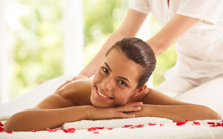 Front view of a happy and relaxed woman receiving back massage at spa, surrounded by rose petals. Front view of a happy and relaxed woman receiving back massage at spa, surrounded by rose petals.