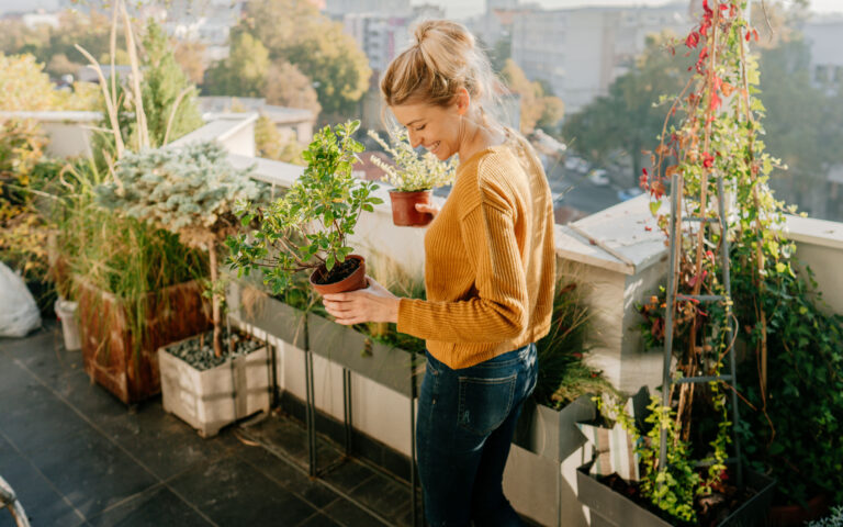 Photo of young woman taking care of her plants on a rooftop garden