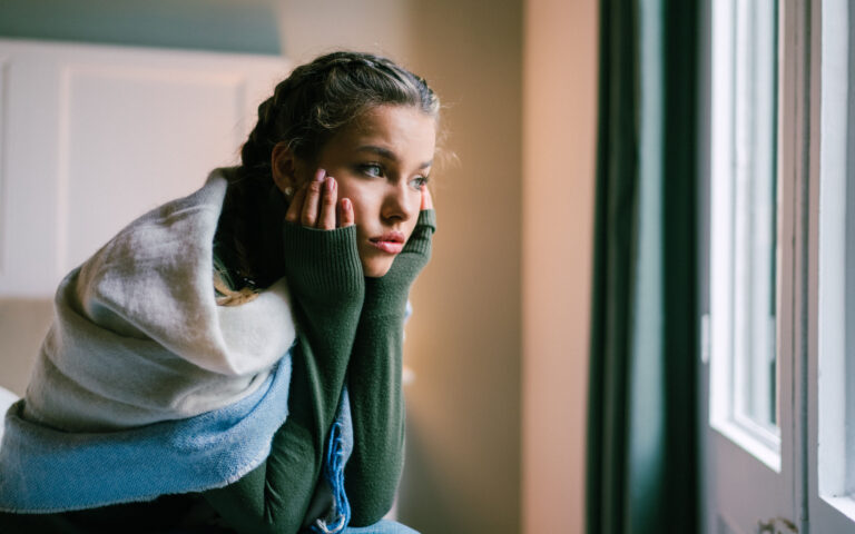 Young woman sitting at the bed and looking through the window