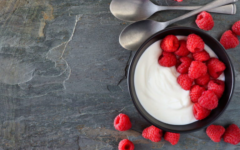 Bowl of yogurt with raspberries. Top view, side border on a dark slate background. Copy space. Bowl of yogurt with raspberries. Top view, side border on a dark slate background. Copy space.