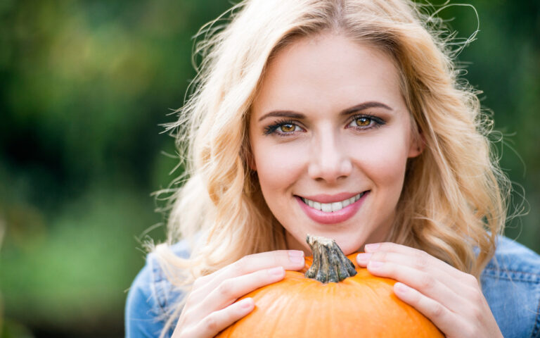 Close up of beautiful young blond woman in denim shirt with orange pumpkin. Autumn nature.