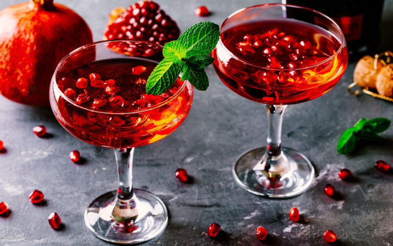 red cocktail with champagne and pomegranate seeds on rustic background