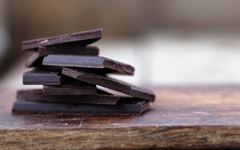 Stack of broken dark chocolate bar pieces on a wooden background. Horizontal