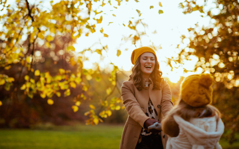 Hello october. smiling modern mother and child in yellow hats outside in the city park in autumn having fun time.