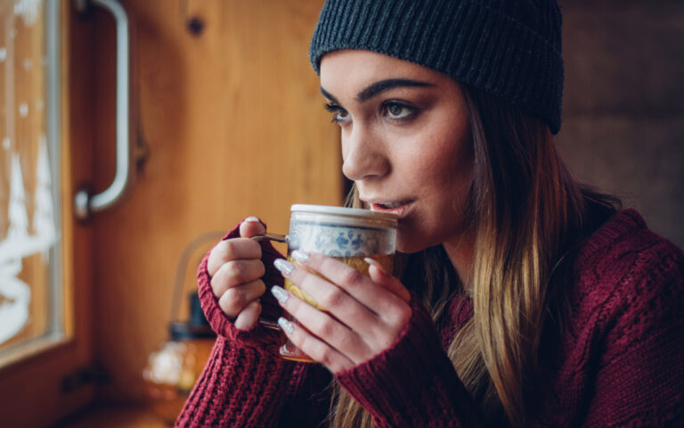 Beautiful young woman with knit hat drinks tea at cafe