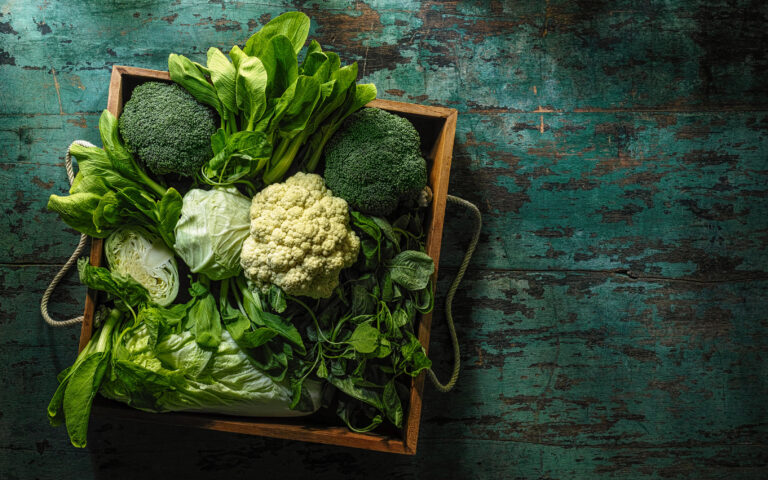 Market fresh green leaf vegetables in an old wooden crate on an old wooden turquoise table. Vegetables include, broccoli, cauliflower, cabbage, spring greens, bok choy and spinach Market fresh green leaf vegetables in an old wooden crate on an old wooden turquoise table. Vegetables include, broccoli, cauliflower, cabbage, spring greens, bok choy and spinach