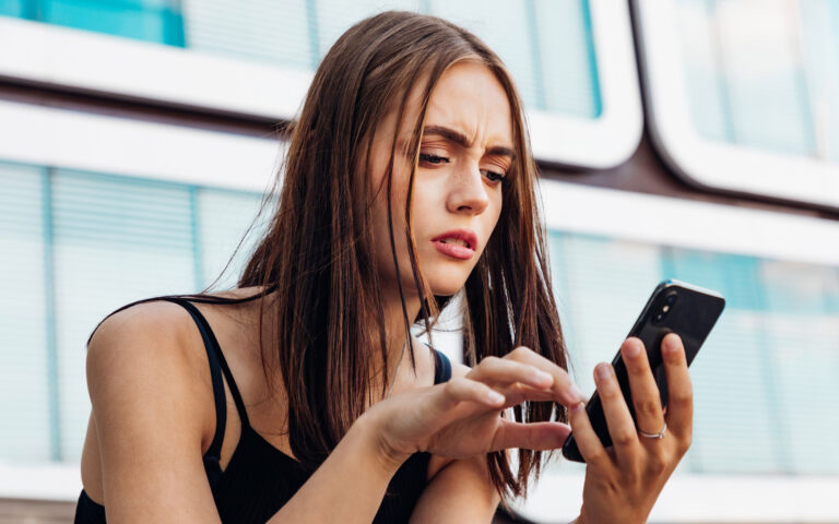Reading Bad News on Mobile Phone. Young teenage woman checking her messages and social media post on her mobile phone. Looking worried and questioning reading the bad news and messages on her smart phone. Urban Young Generation Social Media Lifestyle Portrait. Reading Bad News on Mobile Phone. Young teenage woman checking her messages and social media post on her mobile phone. Looking worried and questioning reading the bad news and messages on her smart phone. Urban Young Generation Social Media Lifestyle Portrait.