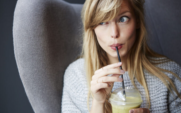 Beautiful young blond woman with smoothie in cafe, looking away