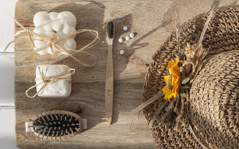 shampo solido, sapone, spazzola per i capelli in legno, spazzolino in bambu, dentifricio in pastiglie e cappello di paglia su tagliere di legno