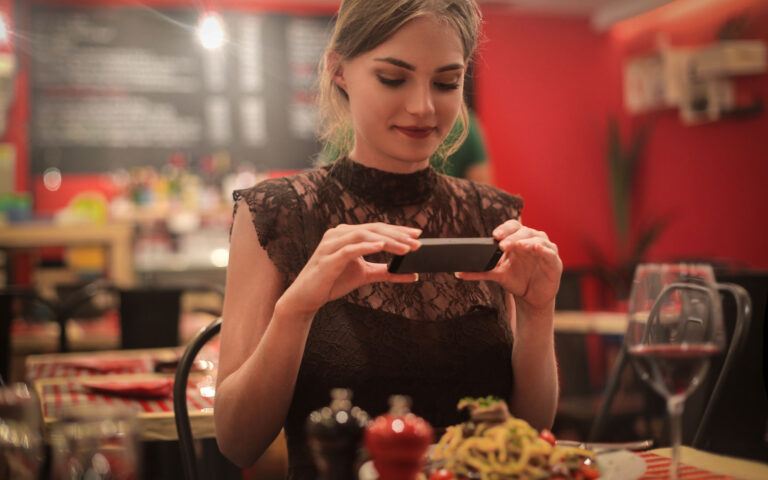 Beautiful girl in black dress taking picture of her food in a restaurant Beautiful girl in black dress taking picture of her food in a restaurant