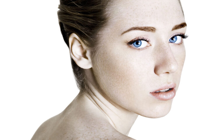 Gorgeous redhead with stunning blue eyes, freckles and perfect skin looking over her shoulder.