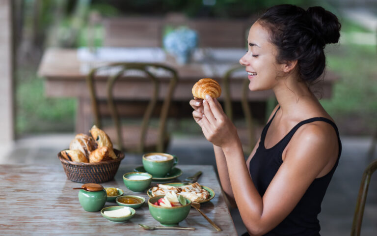 Young woman having breakfast and holding croissant in hand. Morning good mood Young woman having breakfast and holding croissant in hand. Morning good mood