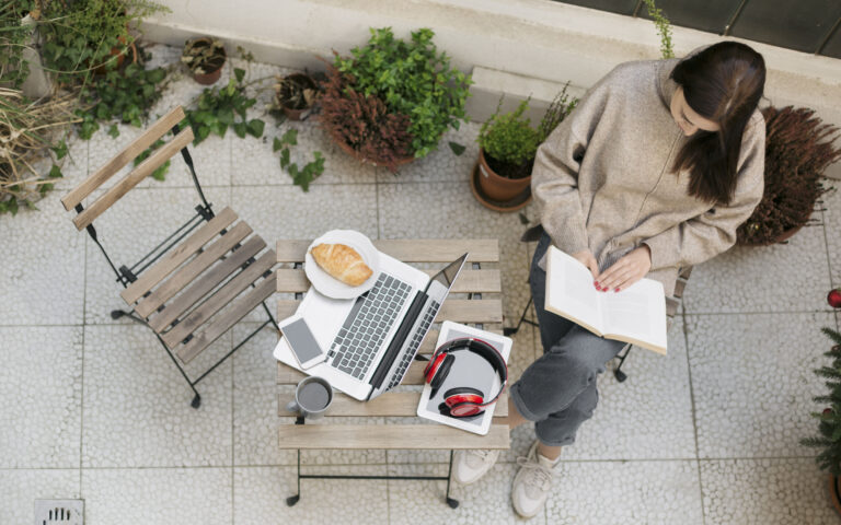 Aerial view of a beautiful young woman reading a book on her apartment balcony feeling relaxed and cozy Aerial view of a beautiful young woman reading a book on her apartment balcony feeling relaxed and cozy
