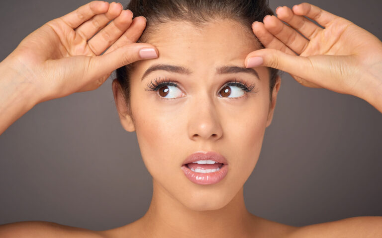 Studio portrait of a beautiful young woman concerned about forehead wrinkles against a gray background Studio portrait of a beautiful young woman concerned about forehead wrinkles against a gray background