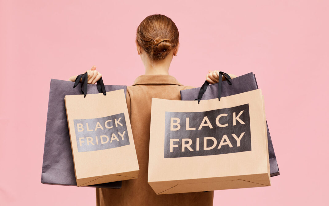Black fridayable woman with hair bun carrying black Friday paperbags on shoulders while leaving store Black friday