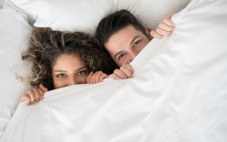 Portrait of a happy couple in the bed covering with the duvet and looking very playful Portrait of a happy couple in the bed covering with the duvet and looking very playful