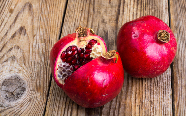Whole and half-cut pomegranate on wooden table. Studio Photo Whole and half-cut pomegranate on wooden table. Studio Photo
