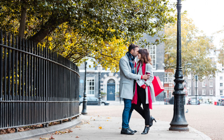 Happy couple embracing on the London street, woman holding shopping bags. Autumn season.