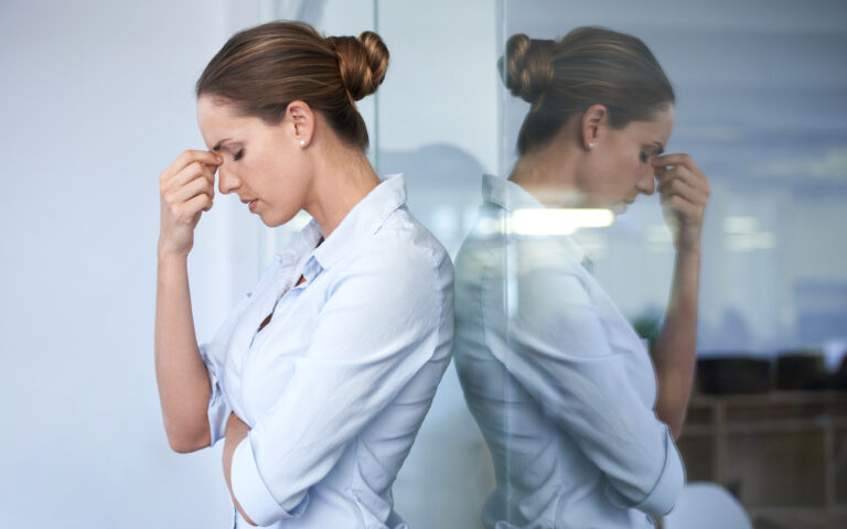 A young businesswoman standing against a glass wall with her head in her hand A young businesswoman standing against a glass wall with her head in her hand