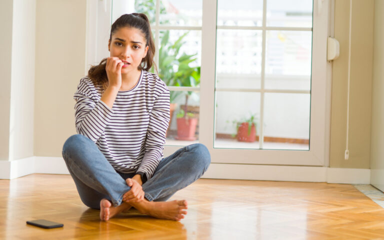 Young beautiful woman sitting on the floor at home looking stressed and nervous with hands on mouth biting nails. Anxiety problem. Young beautiful woman sitting on the floor at home looking stressed and nervous with hands on mouth biting nails. Anxiety problem.
