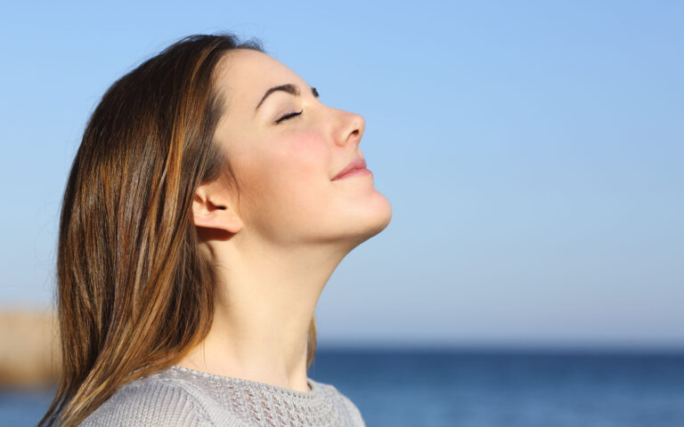 Woman profile portrait breathing deep fresh air on the beach with the ocean in the background Woman profile portrait breathing deep fresh air on the beach with the ocean in the background