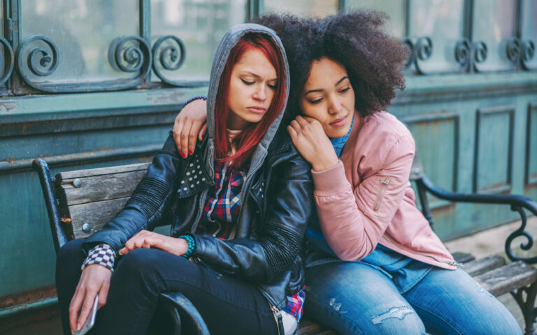 Depressed teenage girl with friend sitting on bench Depressed teenage girl with friend sitting on bench