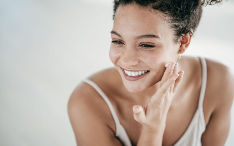 Smiling young women applying moisturiser to her face Smiling young women applying moisturiser to her face