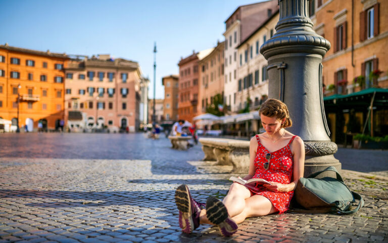 Rome, Italy, August 13 -- A young woman enjoys the quiet of Rome while reading a book sitting on the pavement of Piazza Navona, in the baroque heart of the Eternal City. Piazza Navona is much loved by tourists for the presence of numerous typical restaurants and for the monumental and artistic treasures of one of the most famous squares in the world, where you can experience the essence and soul of Roman life. In the background the Fountain of the Four Rivers by Gian Lorenzo Bernini and the facade of the church of Sant'Agnese by Francesco Borromini. In 1980 the historic center of Rome was declared a World Heritage Site by Unesco. Image in high definition format. Rome, Italy, August 13 -- A young woman enjoys the quiet of Rome while reading a book sitting on the pavement of Piazza Navona, in the baroque heart of the Eternal City. Piazza Navona is much loved by tourists for the presence of numerous typical restaurants and for the monumental and artistic treasures of one of the most famous squares in the world, where you can experience the essence and soul of Roman life. In the background the Fountain of the Four Rivers by Gian Lorenzo Bernini and the facade of the church of Sant'Agnese by Francesco Borromini. In 1980 the historic center of Rome was declared a World Heritage Site by Unesco. Image in high definition format.