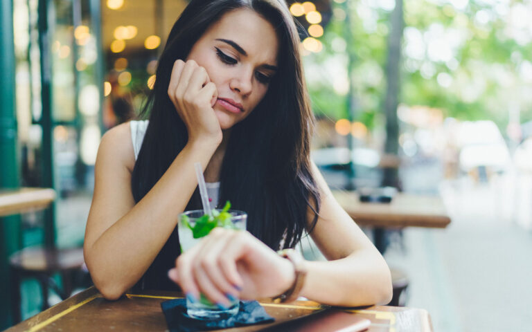 Young woman drinking cocktail at sidewalk cafe and checking the time Young woman drinking cocktail at sidewalk cafe and checking the time