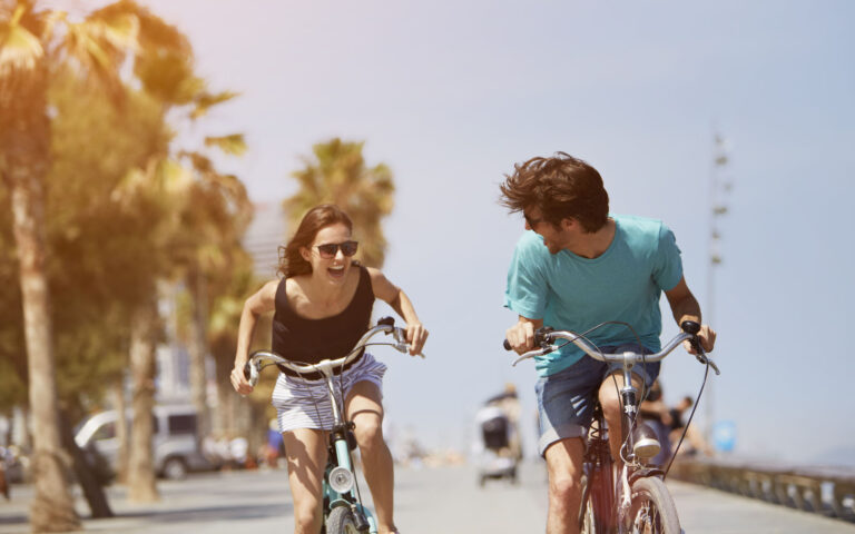Happy young woman chasing man while riding bicycle during summer vacation Happy young woman chasing man while riding bicycle during summer vacation
