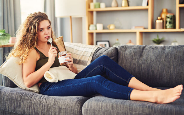 Shot of a young woman eating chocolate from a jar with a hot water bottle over her stomach Shot of a young woman eating chocolate from a jar with a hot water bottle over her stomach