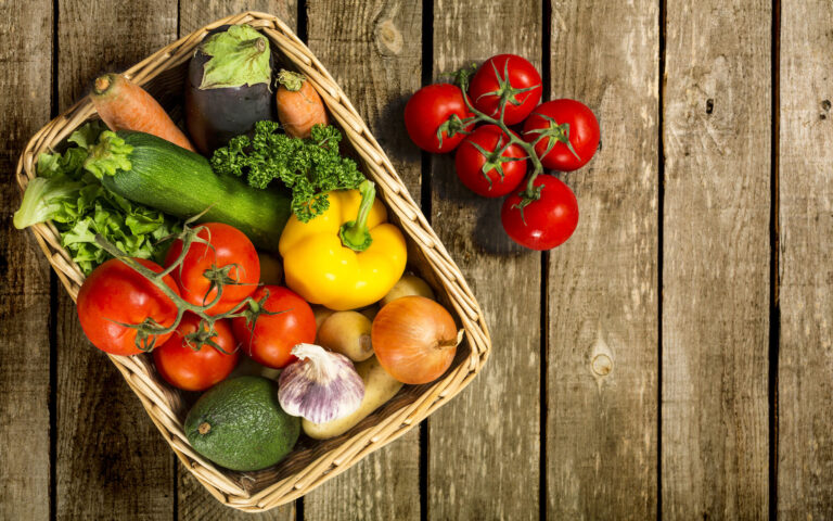 View directly above of a bunch of fresh vegetables in a basket and sitting on a weathered wooden table. Studio shot and plenty of copy space. View directly above of a bunch of fresh vegetables in a basket and sitting on a weathered wooden table. Studio shot and plenty of copy space.