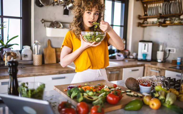 Photo of happy beautiful young woman while she try tasty vegan salad in the kitchen at home. Photo of happy beautiful young woman while she try tasty vegan salad in the kitchen at home.