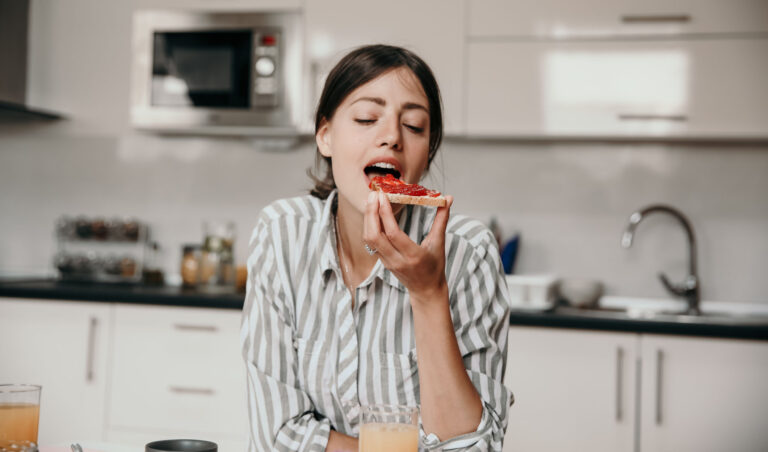 Portrait of a beautiful young woman having her toast with jam, wearing a striped shirt, ready  to enjoy the bite. Breakfast concept
