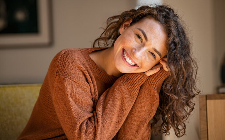 Happy young woman sitting on sofa at home and looking at camera. Portrait of comfortable woman in winter clothes relaxing on armchair. Portrait of beautiful girl smiling and relaxing during autumn. Happy young woman sitting on sofa at home and looking at camera. Portrait of comfortable woman in winter clothes relaxing on armchair. Portrait of beautiful girl smiling and relaxing during autumn.