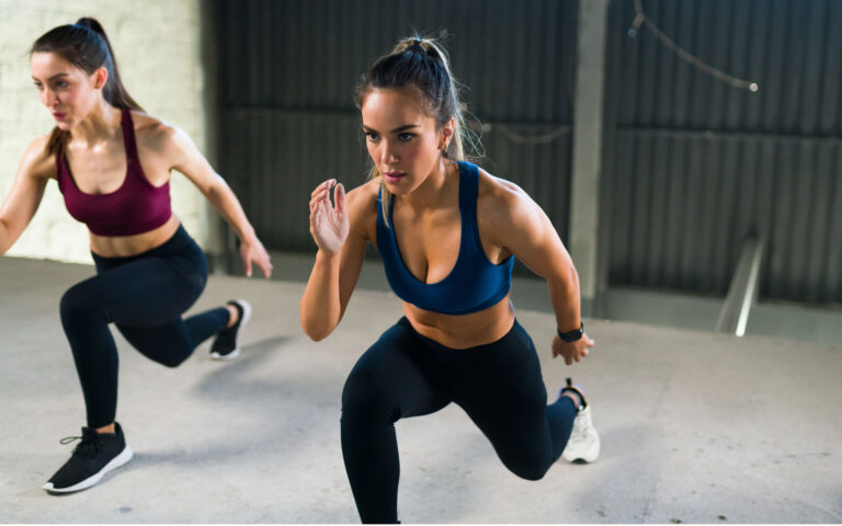 Athletic young woman with a healthy lifestyle doing leg lunges during a HIIT class. Women working out together at the fitness center Athletic young woman with a healthy lifestyle doing leg lunges during a HIIT class. Women working out together at the fitness center