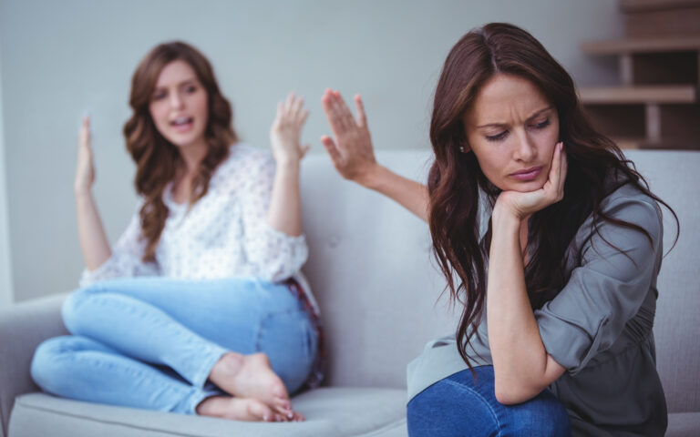 Two female friends sitting on sofa and arguing with each other Two female friends sitting on sofa and arguing with each other
