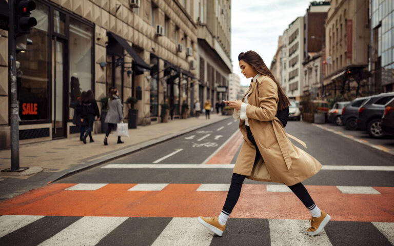 Beautiful young woman looking bothered, texting on her phone while crossing the street