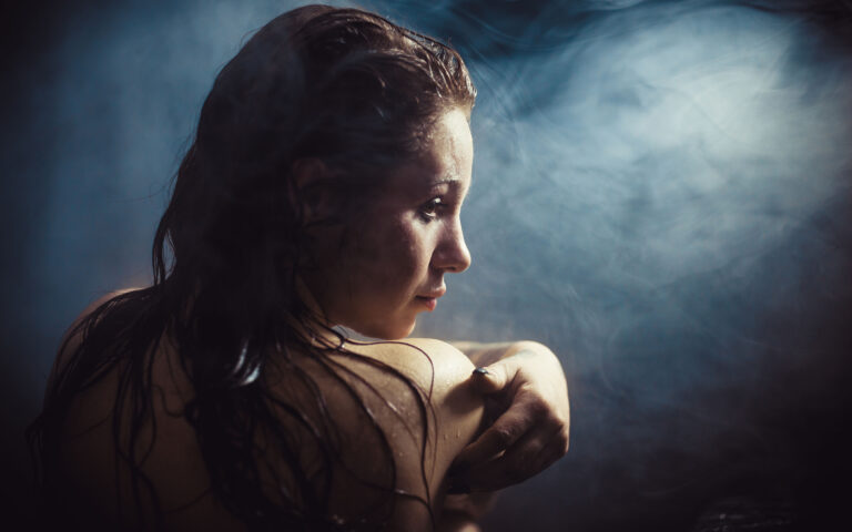 Woman with a wet body sitting in a dark steamy bathroom Woman with a wet body sitting in a dark steamy bathroom