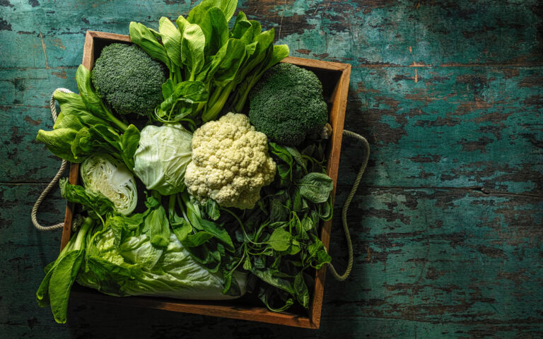 Market fresh green leaf vegetables in an old wooden crate on an old wooden turquoise table. Vegetables include, broccoli, cauliflower, cabbage, spring greens, bok choy and spinach Market fresh green leaf vegetables in an old wooden crate on an old wooden turquoise table. Vegetables include, broccoli, cauliflower, cabbage, spring greens, bok choy and spinach