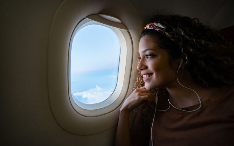 Portrait of a happy woman traveling by plane and listening to music with headphones while looking through the window - lifestyle concepts