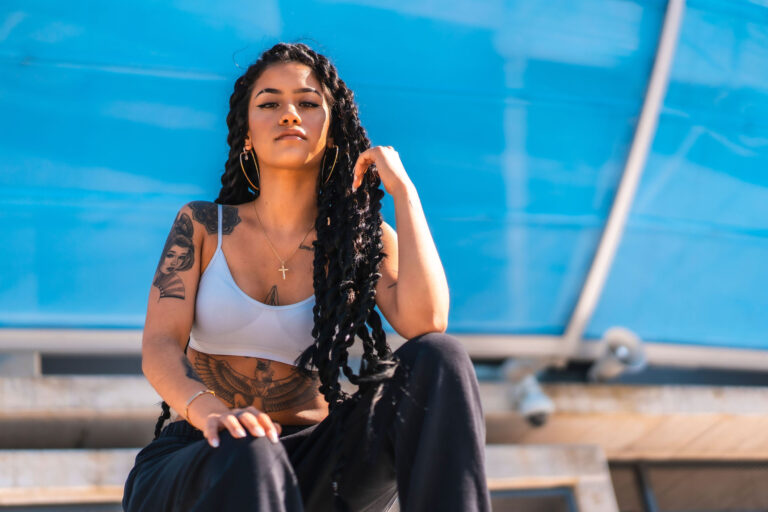 A young Hispanic woman with long braids and tattoos posing under the sunlight