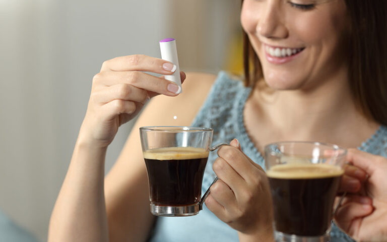 Close up of a woman hand throwing saccharine into a coffee cup sitting on a couch in the living room at home