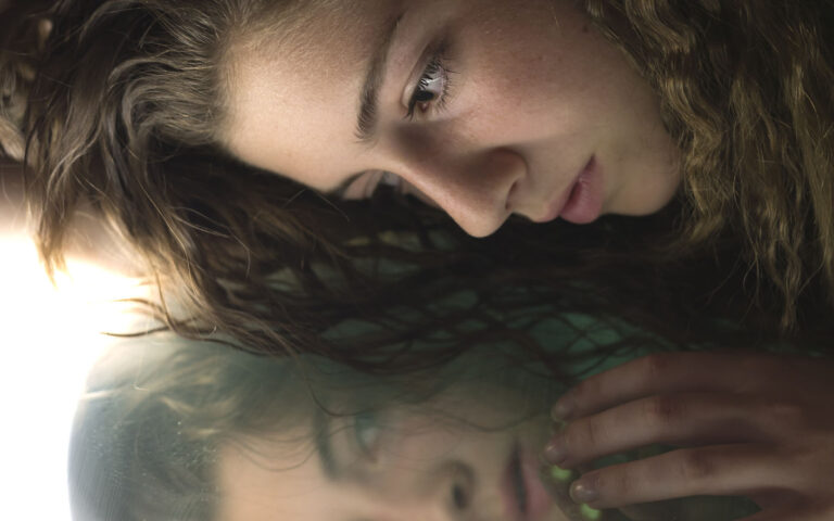 Teenage woman looking at herself in a mirror with serious face.